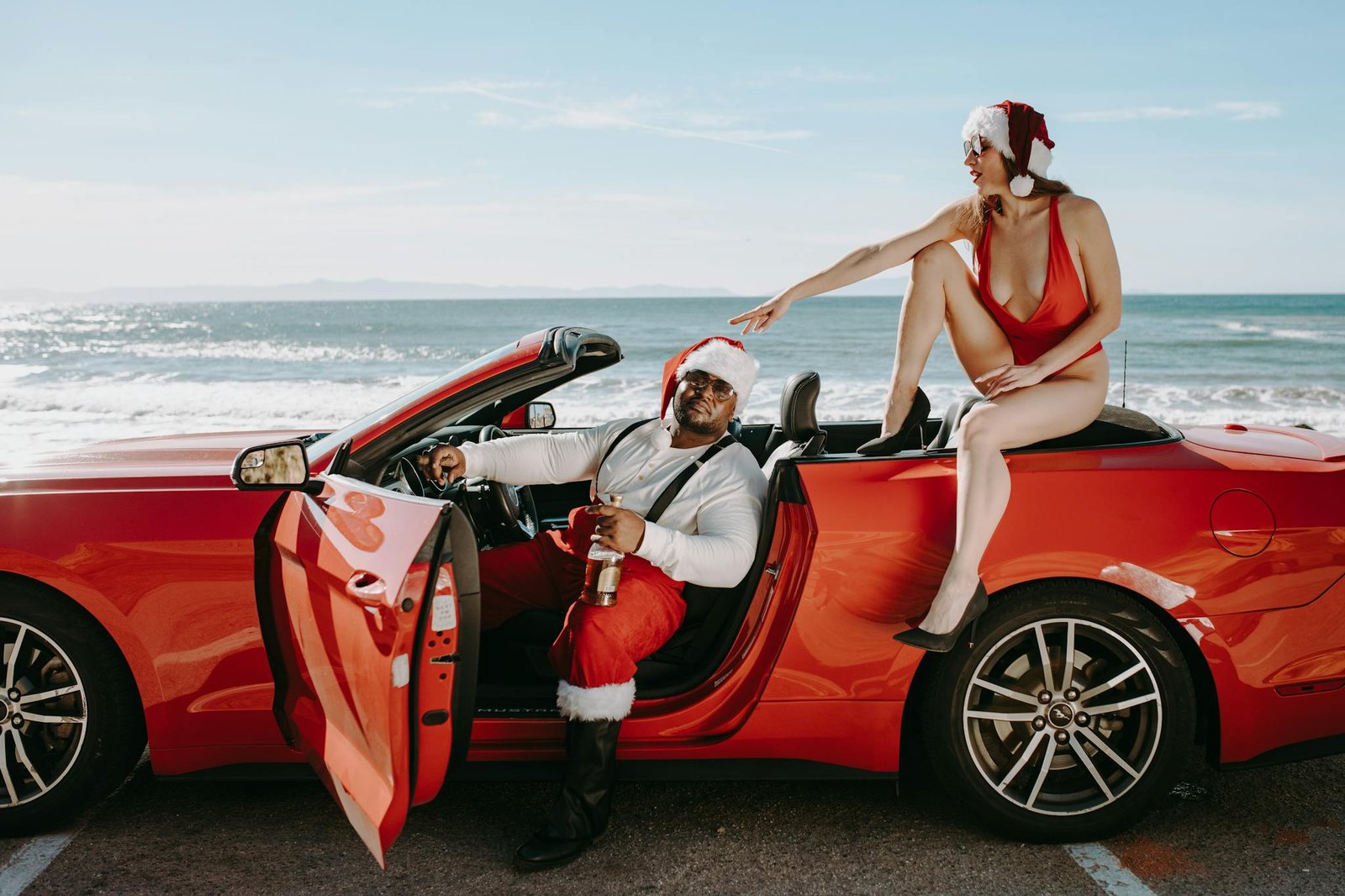 Festive Santa and friend enjoying beach vibes with a red convertible in a fun holiday setting.